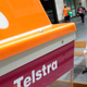 A man uses a mobile device while sitting near a Telstra public telephone in Sydney on Oct. 25, 2021.